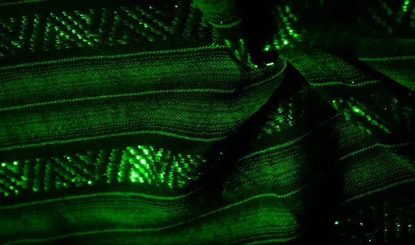 Yeşil ışıkla aydınlatılan katmanlı ve karmaşık desenli yeşil kumaş. Parıltı kumaşın dokusunu vurguluyor. Bu da materyalin içinde organik ve sıvı bir şekil ortaya çıkarıyor..