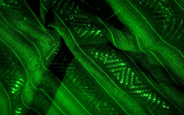 Geometrik desenlerle örülmüş yeşil kumaş kıvrımlarını bulanıklaştırır. Parlayan ışıklarla hafifçe aydınlatılır. Boyut ve derinlik dolu akışkan ve hipnotik bir soyut tasarım yaratır..