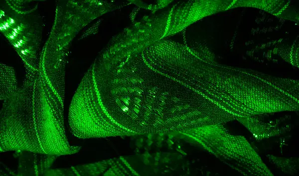 Yumuşak dalgalarda parlayan yeşil kumaş bulanıklığı ve karmaşık parlak desenler. Kumaş kıvrımları dinamik ışık yansımaları yaratarak büyüleyici bir doku etkisi yaratıyor..