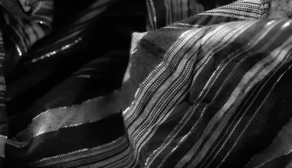 Görüntü, parlak siyah kumaş ve dikey parlak çizgiler. Katlanmış malzeme ışığı güzel bir şekilde yakalıyor, karmaşık dokuma detaylarını gözler önüne seriyor ve tek renkli tonlarda zarif bir kontrast oluşturuyor..