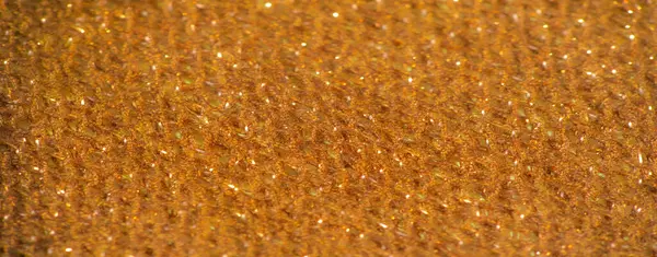 Işıldayan iplikler ve parlak gölgelerle bronz kumaşın bulanık yakın çekimi. Materyalin yumuşak kıvrımları ışığı yakalıyor, varlıklı ve sofistike bir görünüm yaratıyor..