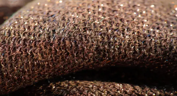 Yüzeyinde karmaşık bir parıltı olan parlak kahverengi kumaş bulanıklığı. Kumaş, ışığı yumuşak bir ışıltıyla yansıtıyor, malzeme dokusu ve tasarımı sergiliyor. Zarif, ışıltılı detaylar göze çarpıyor.