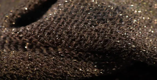 Metalik ipliklerle birbirine karışmış koyu dokulu bir kumaş bulanıklığı. Işığı yüzeyine yansıtıyor. Işıldayan dokuma, dinamik ve ışıltılı bir desen oluşturur.