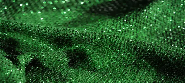 Karmaşık parlak dokusu olan yeşil kumaştan bulanık, düşük ışık altında hafif ve parıltılı, üst düzey moda tasarımı için mükemmel görsel dinamik bir tekstil sahnesi yaratıyor..