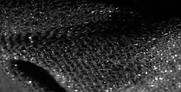 Siyah parıldayan kumaşın detaylı bir makro görüntüsü. Karmaşık dokumayı ve ışıkta parlayan yansıtıcı elementleri vurguluyor. Doku zengin ve lüks.