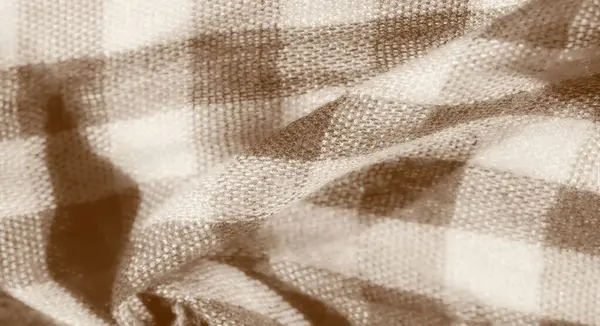 Katlanmış ve toplanmış bej ve kahverengi damalı kumaşın bulanıklığı. Kumaşın yumuşak ve dokulu bir görüntüsü var. Sade ve sade cazibesini vurguluyor..
