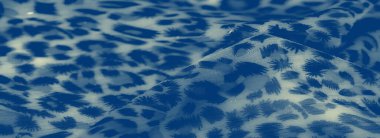 Görüntü, soyut, organik desenlere sahip, narin, şeffaf bir mavi kumaş, yaban yaprağı ve leopar deseni anımsatıyor, arka planda yavaşça bulanıklaşıyor. n.