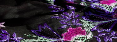 Çiçek desenli bulanık pembe, yeşil ve mor renkli yumuşak siyah kumaş. Karmaşık yapraklar ve taç yaprakları derin arka planda güzel bir kontrast oluşturuyor..