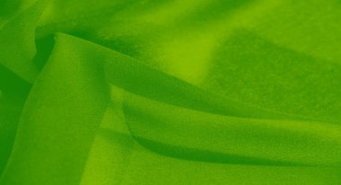 Bulanık, yeşil kumaş yumuşak dalgalar halinde akar, yumuşak gölgeleri dokulu yüzeyi boyunca akar. Zengin, koyu yeşil renk kumaşın zarafetini ve pürüzsüz kalitesini arttırır..