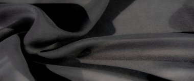 Siyah kumaşın yakın plan görüntüsü, gölgeleri ve görüntüye derinlik ve hareket katlayan nazik kıvrımlarını ortaya çıkarır. Yumuşak kıvrımlar kumaşın gelişmişliğini arttırır.
