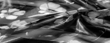 Bulanık, dikey çiçek desenli gri tonlu kumaş narin çiçekler ve katmanlı dokular sergiliyor. Işığın ve gölgenin yumuşak etkileşimi uyumlu bir tasarım yaratır..