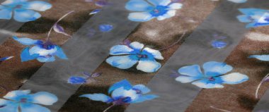 Görüntü. Mavi ve siyah tonlarında narin kumaşlar, mavi ve mavi çiçekli desenlerle süslenmiş. Işık yansımaları maddeye metalik bir parlaklık ekler ve lüks bir doku yaratır.