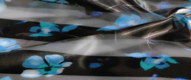 Parlak, koyu arkaplanda mavi renkleri olan narin çiçekli kumaşın bulanıklığı ince kıvrımlar ve parlaklıkla zarif ve sofistike bir doku yaratıyor..