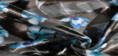 Mavi çiçek aksanlı saf kumaş bulanıklığı. Karmaşık kıvrımlar ve hafif oyunlar. Şeffaflık çiçek detaylarını mavi ve yumuşak mor renklerin karışımıyla ön plana çıkarıyor. .