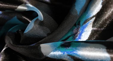 Karanlık ve aydınlık katmanların bir karışımı parlak bir kumaş üzerinde canlı mavi çiçek aksanları sergiliyor, yumuşak, akıcı çizgiler ve karmaşık desenlerle zarif ve sakin bir görünüm yakalıyor..