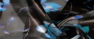 Bulanık katlanmış kumaş, zarif çiçek aksanıyla koyu arkaplanda mavi ve mor tonlarda, ışığı yakalayan hassas, akıcı bir doku yaratıyor..