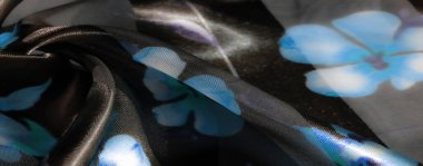 Koyu bir tabanda mavi çiçekli bulanık kumaş, güzel katmanlı ve desenli, ışık yansıtan bir yüzey, zarafeti yakalıyor..