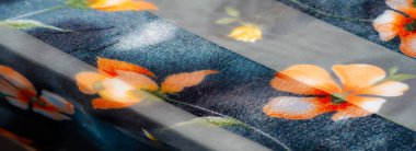 Yumuşak, şeffaf katmanları ve ince çiçek aksanıyla bu kumaş zarafet yayıyor. Turuncu ve sarı çiçekler pürüzsüz, siyah bantlara karşı duruyorlar. Tasarıma ince bir dokunuş katıyorlar.