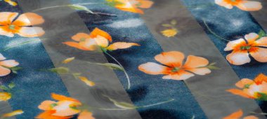 Bu yakın plan kumaş, turuncu ve sarı renkli çiçek desenli parıldayan bir doku sergiliyor. Nazik katlama ve katlama yumuşak, zarif bir estetik yaratıyor. Tekstil tasarımı için mükemmel..