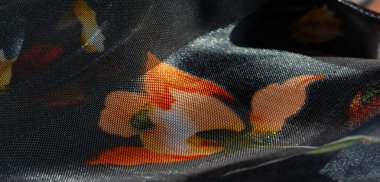 Koyu mavi bir tabanda turuncu ve sarı çiçek izleriyle parıldayan saf kumaş bulanıklığı. Kumaşlar parlak ve narin katlar ince, yumuşak bir estetiği çağrıştırıyor. .