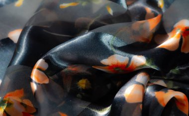 Parlak turuncu çiçek desenli bulanık kumaş. Karanlık, parlak bir arkaplan üzerine kurulmuş. Karmaşık kıvrımlar ve parıldayan yüzey boyunca ince bir ışık oyunu.