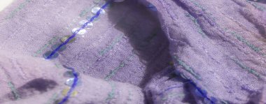 Hassas pullarla süslenmiş soluk mor bir kumaş. Yeşil ve mavi dikişli çizgiler boyunca dizilmiş. Yumuşak, katlanmış yüzeylerde ince bir doku oluşturuyor..