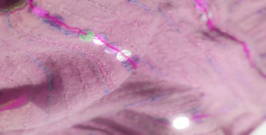 Mor dikişler ve pullarla süslenmiş pembe kumaşın yakın görüntüsü büyüleyici, narin ve zarif bir zarafetle yumuşak, lüks bir doku sunuyor..