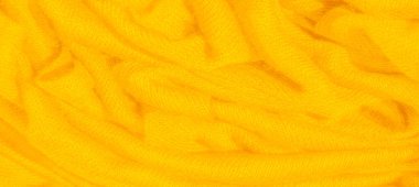 Dokulu, katlanmış görünümlü canlı sarı kumaş bulanıklığı, doğal gölgeler ve röflelerle görsel olarak zengin bir zemin oluşturuyor. Katlar hareket ve sıcaklık hissi veriyor.