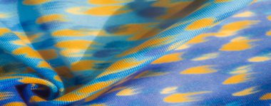 Mavi kumaş bulanıklığı, parlak turuncu detaylar ve soyut desenler. Kumaşın pürüzsüz dokusu ve yumuşak kıvrımları dinamik bir havayla modern bir görünüm yaratır.