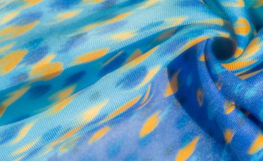 Mavi kumaş bulanıklığı, parlak turuncu detaylar ve soyut desenler. Kumaşın pürüzsüz dokusu ve yumuşak kıvrımları dinamik bir havayla modern bir görünüm yaratır.