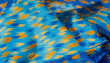 Soyut sarı ve mor benekli mavi bir kumaşın bulanık görüntüsü yumuşak kıvrımlardaki ışık ve gölgenin etkileşimini yakalıyor. Lekeler, fırça darbesi izi gibi görünüyor.,