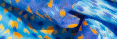 Mavi ve turuncu soyut desenlerin bulanıklığı dinamik ve canlı bir doku yaratıyor. Kumaş yumuşak, pürüzsüz kıvrımlar halinde akar, hassas fırça darbeleri gibi görünen renklerin enerjik bir karışımını gösterir.