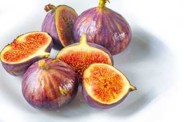 Küçük bir incir grubu, bazıları canlı kırmızı, tohumlu eti ortaya çıkarmak için dilimlenmiş, bu besleyici, egzotik meyvenin renk ve dokusundaki çeşitliliği gözler önüne seriyor..