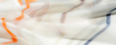 Ilık turuncu ve gri tonlarda şeffaf kumaşın hassas kıvrımlarını içeren bulanık bir görüntü. Kalıplar ve yumuşak dokular hafif, havadar bir his yaratıyor, sıcaklık ve zarafet hissi uyandırıyor..