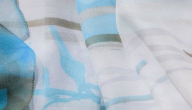 Açık mavi ve bej desenli narin bir kumaşın bulanıklığı ruhani ve havadar bir his yaratıyor. Kumaşın yumuşak örtüsü ince dokuları nazik bir akımla birleştirir..