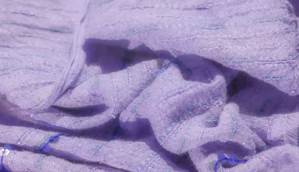 Lavanta desenli kumaş bulanıklığı, dikişli detaylar ve pullu aksanlar, zarif bir ışık oyunu yaratıyor. Mavi iplik derinlik ve ilgi katıyor..