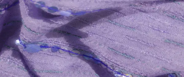 Pul ve ince yeşil ipliklerle renklendirilmiş ince bir parıltıyla mor kumaşın bulanık görüntüsü. Kumaşın dokusu ve kıvrımları yumuşak, lüks bir his veriyor.