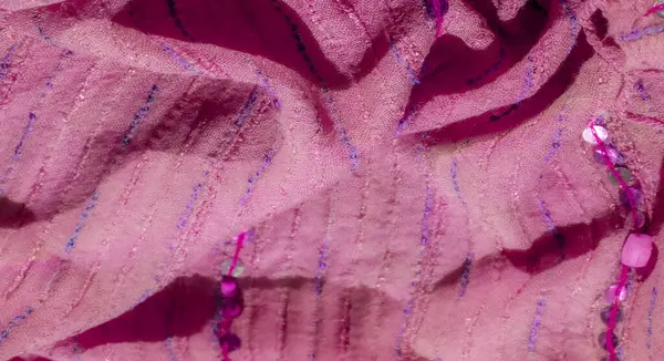 Hassas pullarla süslenmiş bulanık pembe kumaş ve dikişli desenler yumuşak, dokulu bir görünüm yaratır. Mor ipliğin ince ipuçları ve parıldayan pullar derinlik ve zarafet ekler.