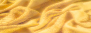 Detaylı dokuma dokuları ve yumuşak kıvrımları olan sarı kumaş bulanıklığı. Kumaşın sıcak tonları ve karmaşık desenleri ortam ışığı altında rahatlık ve zarafet hissi yaratır..