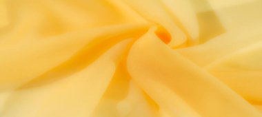 Canlı sarı kumaştan bulanık, nazikçe katlanmış ve kıvrılmış, yumuşak akış çizgileri ve ince gölgeler yaratıyor. Kumaşlar ışığı yansıtıyor.