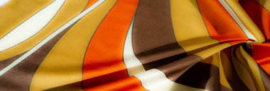 Bulanık turuncu, sarı ve kahverengi çizgili kumaş yumuşak kıvrımlı ve saten gibi pürüzsüz bir dokusu var. Renklerin ve gölgelerin etkileşimi resme derinlik ve sıcaklık ekler