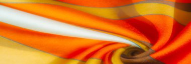 Bulanık turuncu, sarı ve kahverengi çizgili kumaş yumuşak kıvrımlı ve saten gibi pürüzsüz bir dokusu var. Renklerin ve gölgelerin etkileşimi resme derinlik ve sıcaklık ekler