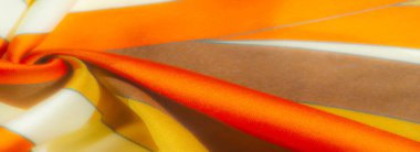 Turuncu, sarı ve kahverengi kumaşlardan oluşan bulanık yakın plan kıvrımlı ve düz saten bir dokusu var. Sıcak tonlar ve akış şekli bir hareket ve derinlik hissi yaratır.