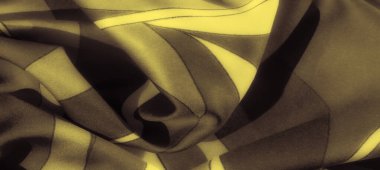 Karanlık bir zemin üzerindeki yumuşak altın dalgaların bulanıklığı katlanmış kumaş üzerinde zarif bir soyut desen oluşturur. Kibar kıvrımlar ve zengin tonlar lüks, dinamik bir görsel yaratıyor..