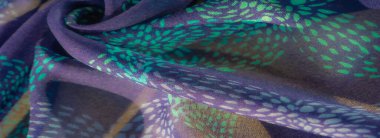 Turkuaz ve deniz mavisi lekeli mor kumaş yakın plan, büyüleyici bir desen oluşturuyor. Kumaşın havadar dokusu ve pürüzsüz kıvrımları rahatlatıcı bir görsel etki yaratır..