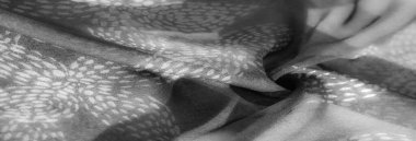 Akan kumaşın gri tonlu yakın plan görüntüsü. Işığın hassas ve soyut bir deseni var. Yumuşak doku ve nazik kıvrımlar gölgelerin ve renklerin sanatsal etkileşimini yaratır.