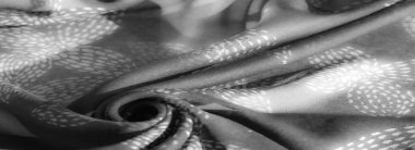 Görüntü. Yapraktan esinlenilmiş, yumuşak ve karmaşık kıvrımlarla kendini saran gri tonlu kumaş. Monokrom tonları dokuyu vurgular ve derinlik hissi yaratır.