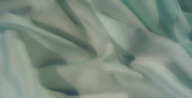 Pürüzsüz pastel yeşil kumaşın kıvrımları ve ince ışıklandırmasıyla bulanıklaşır. Yumuşak malzeme zarafet ve sakinlik yayar, modern, minimalist tasarımlar için mükemmeldir..