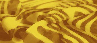 Kalın kahverengi dalgalı desenli, parlak sarı kumaşın bulanık görüntüsü. Karmaşık kıvrımlar modern tekstil tasarımları için ideal yumuşak, soyut bir doku yaratıyor..