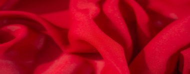 Pürüzsüz, akışkan kıvrımlar halinde yakalanmış kırmızı kumaşların bulanıklığı. Yakın plan, tekstil ve moda tasarımı için ideal yumuşak ve canlı bir dokuyu ortaya çıkarıyor..
